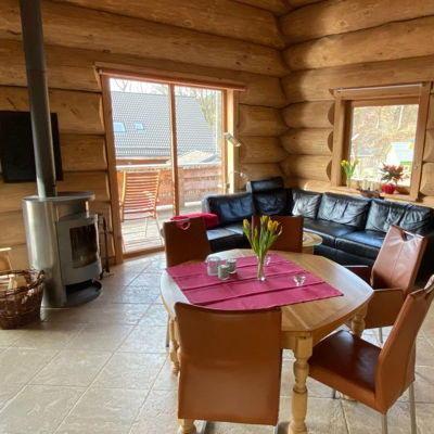 Großes gemütliches Wohnzimmer mit Esstisch und Kaminofen in einem Blockhaus für Feriengäste.
