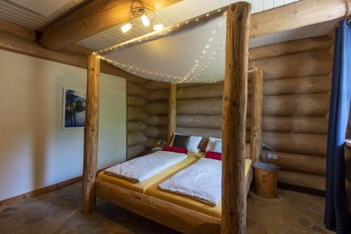 Ein rustikales Himmelbett in einem Blockhaus-Ferienhaus mit sichtbaren Holzstämmen.